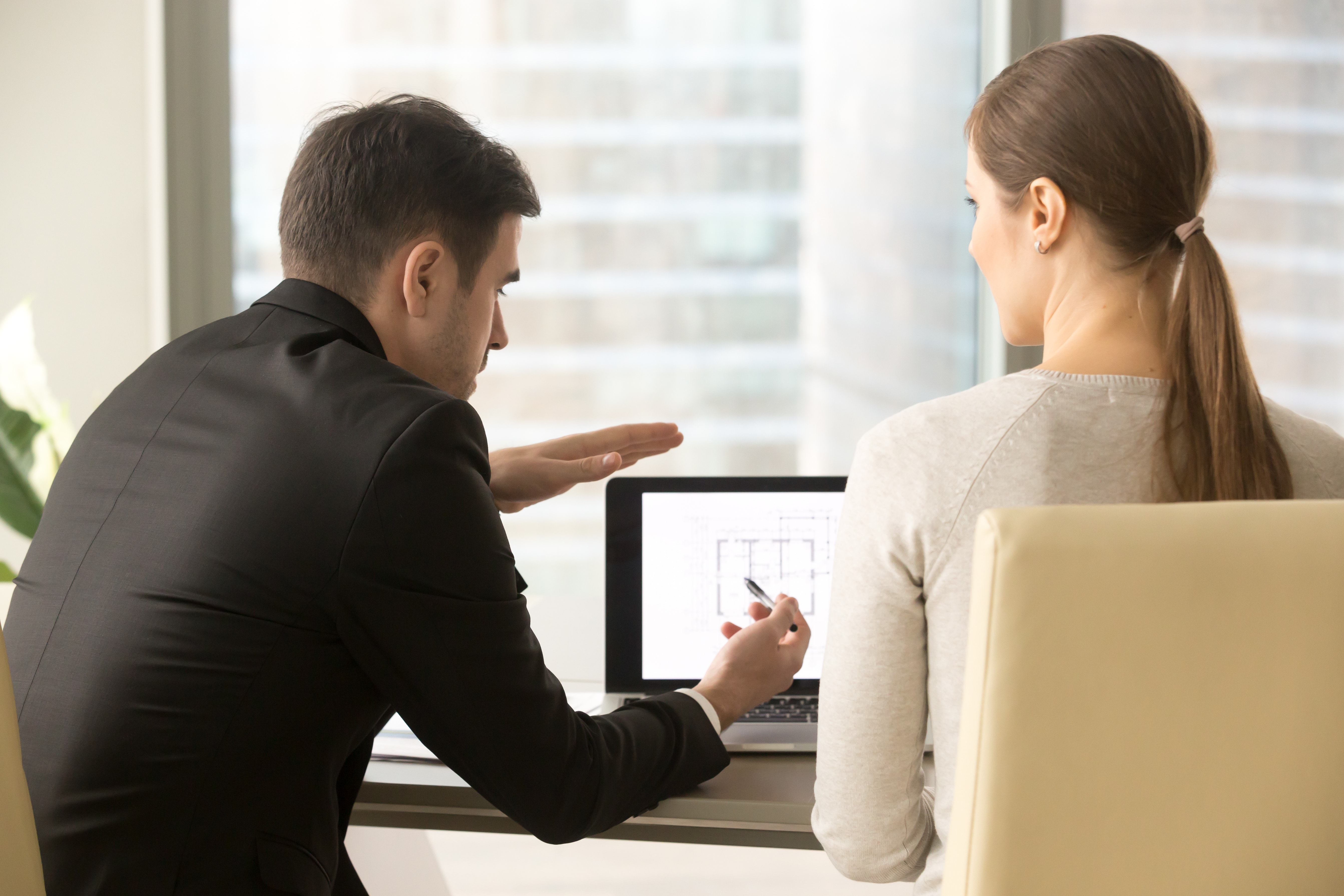 Two people discussing details of design services project while sitting at a desk in front of a laptop with the company floor plan on the screen mapping out the placement of Algo IP endpoints tailored to the company's environment.