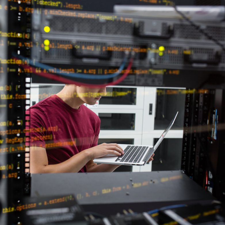 Portrait of modern young man holding laptop standing in server room working with supercomputer